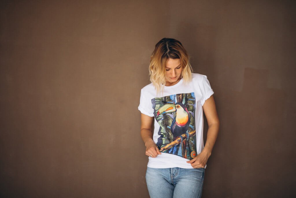 a blonde woman wearing a white shirt with a printed art of a bird