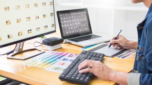 Person typing on a desktop computer while using a drawing pad and a laptop